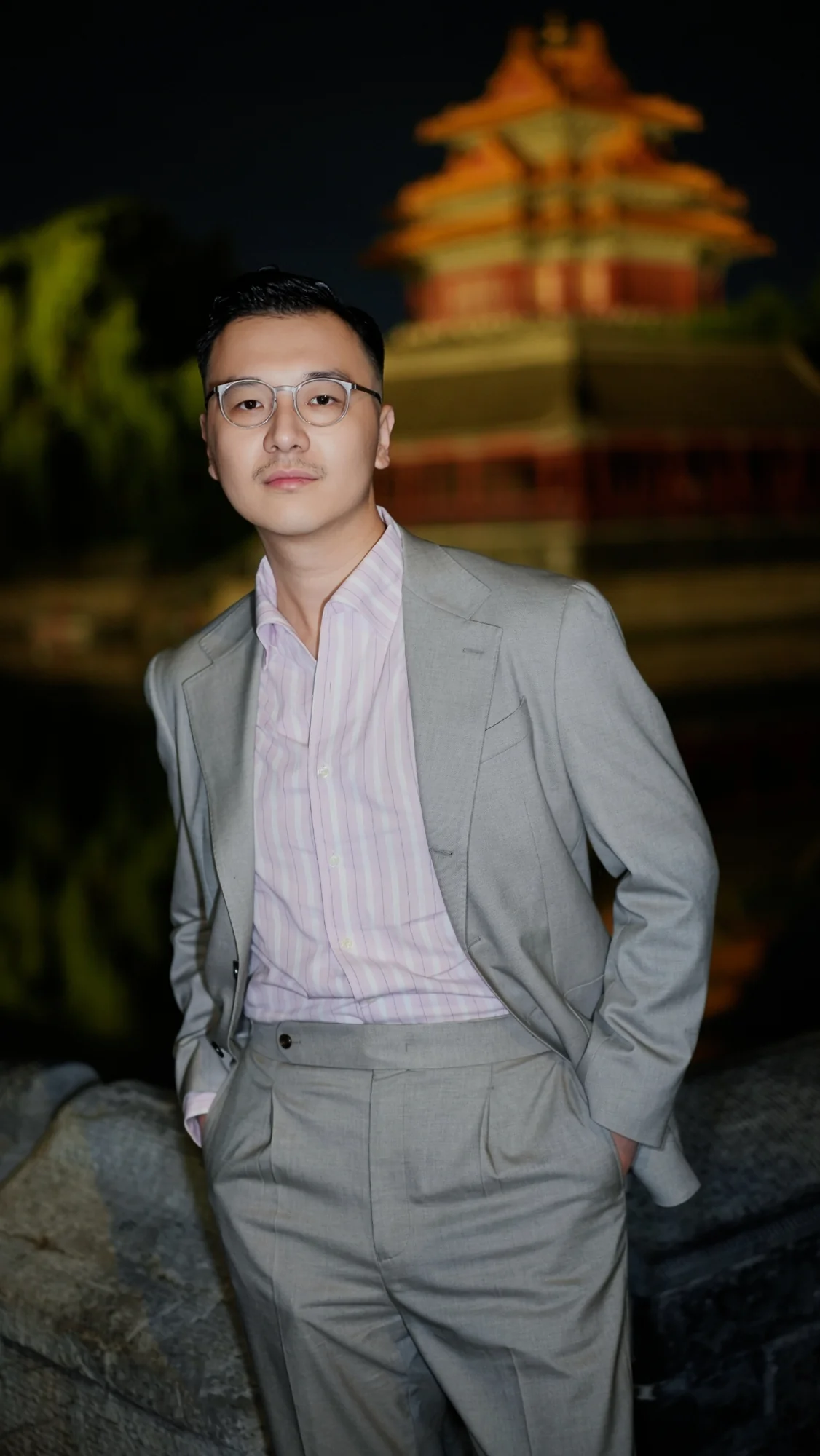 彭勃穿灰色西装，身后是夜间的建筑